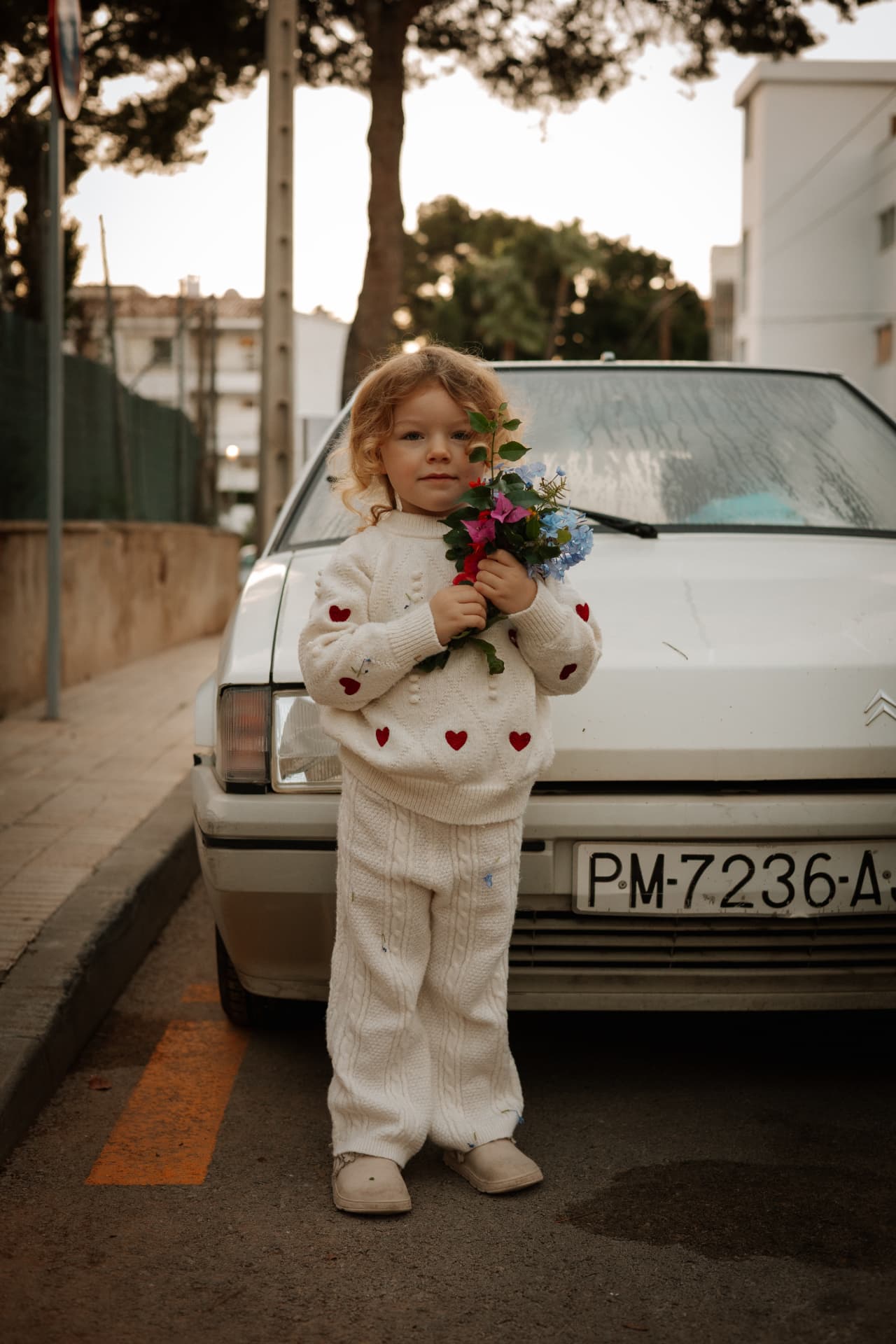 Kind met bloemen voor een oude witte auto