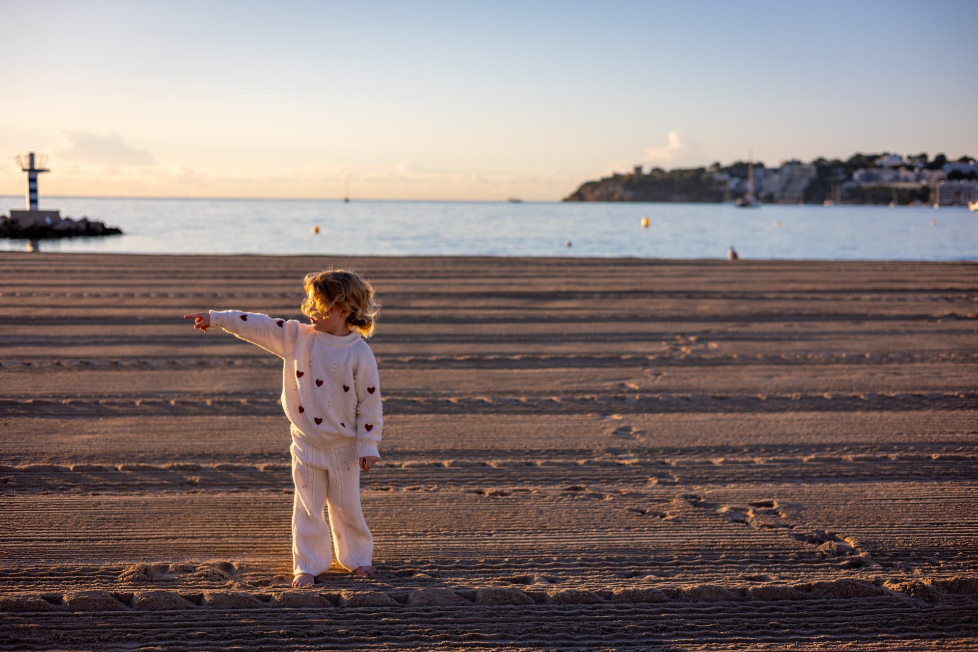 Kind wijst naar de zee op een leeg strand bij zonsondergang