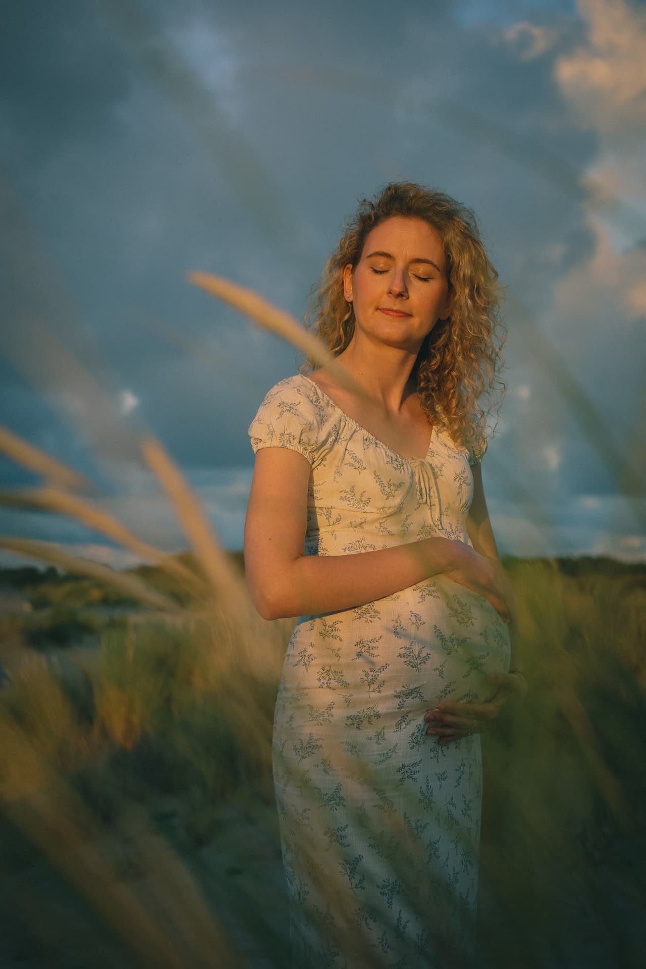 Zwangere vrouw in het duingras bij avondlicht